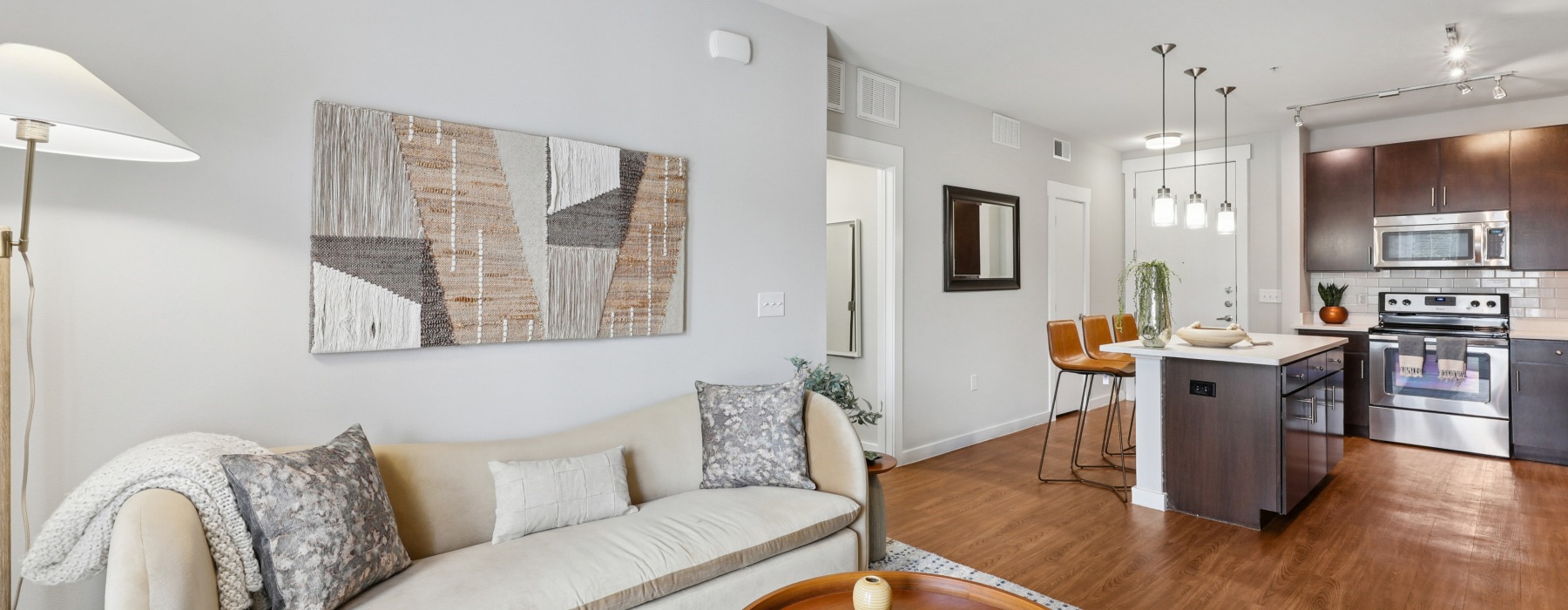 Spacious and well lit living room with wood floors and a large window with access to the kitchen